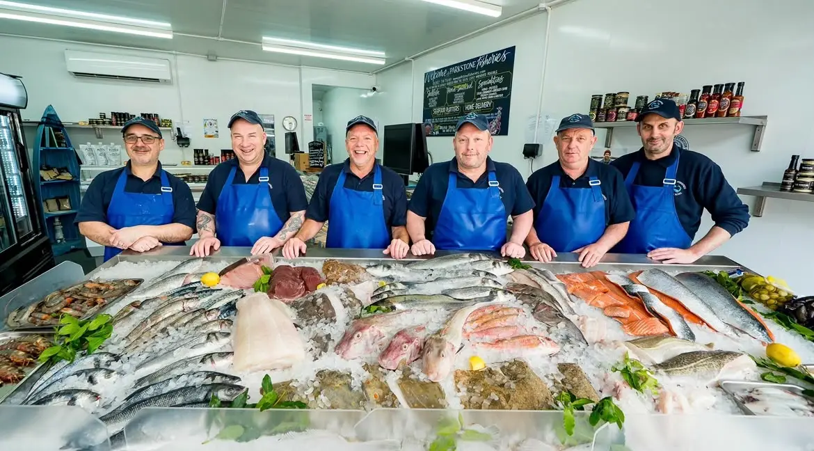 The Parkstone Fisheries team in blue aprons behind a full counter of fresh fish on ice