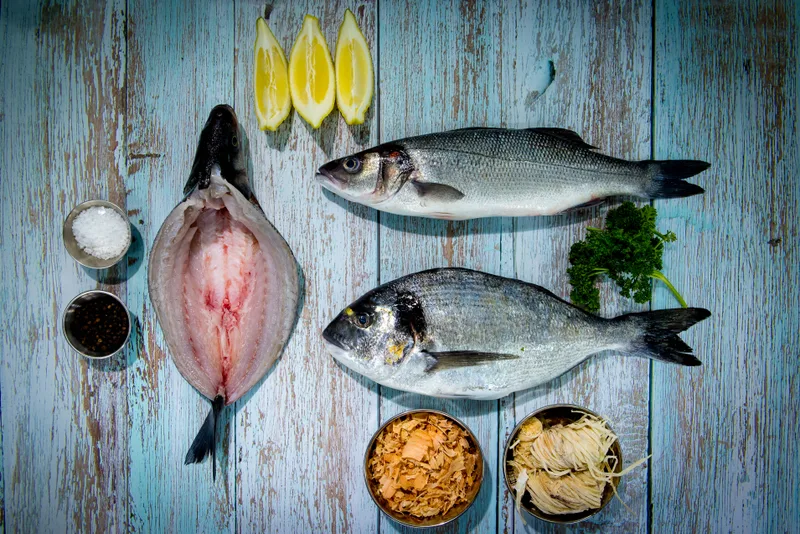 A butterflied fish beside a whole bass and a whole bream, with lemon and herbs