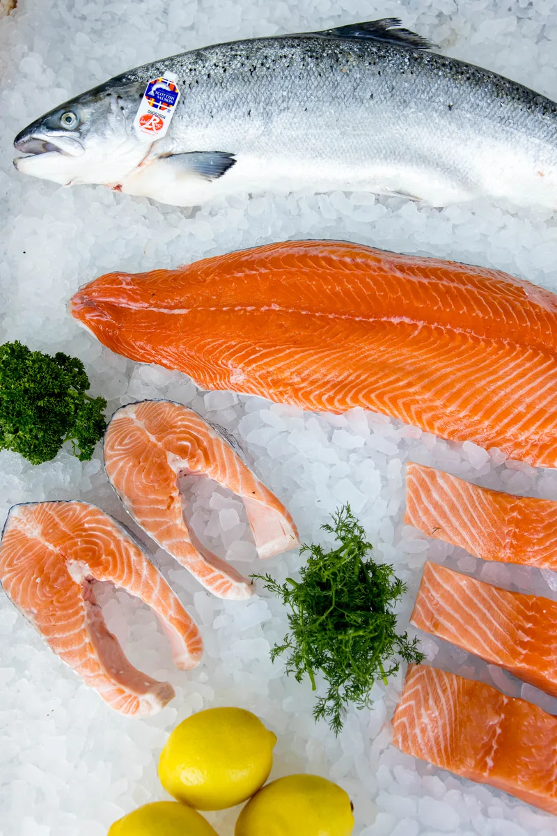 A whole salmon on crushed ice with a skinless side, salmon steaks and fillet portions, lemons and herbs